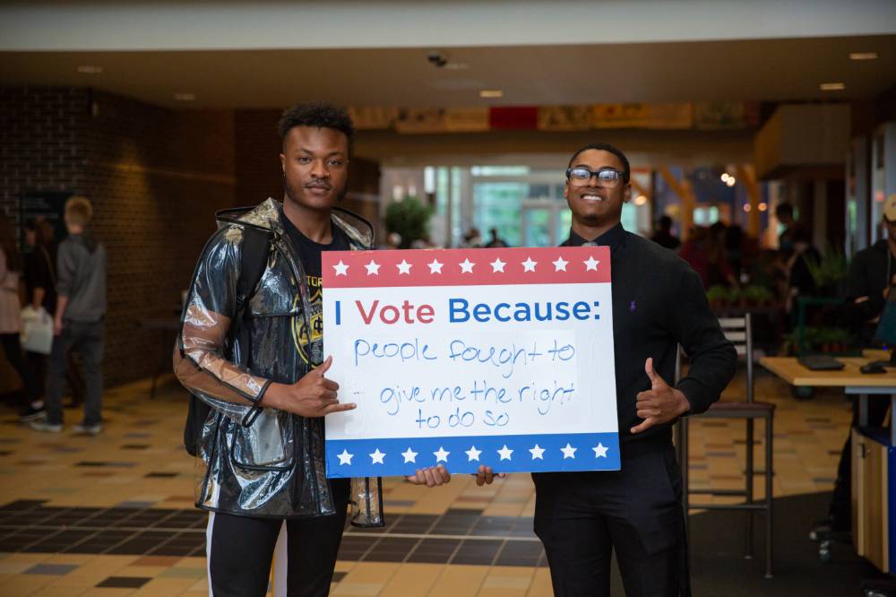 Two GVSU students holding sign titled "I vote because: people fought to give me the right to do so"